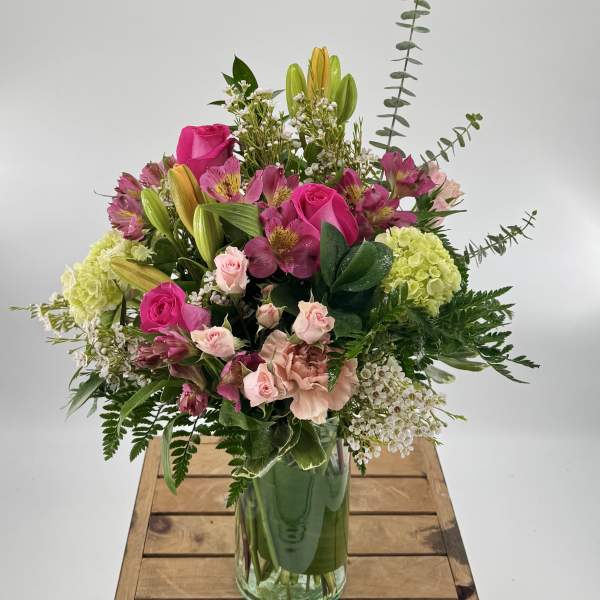 Tall mixed bouquet with pink roses, lilies, and green hydrangeas in a clear glass vase
