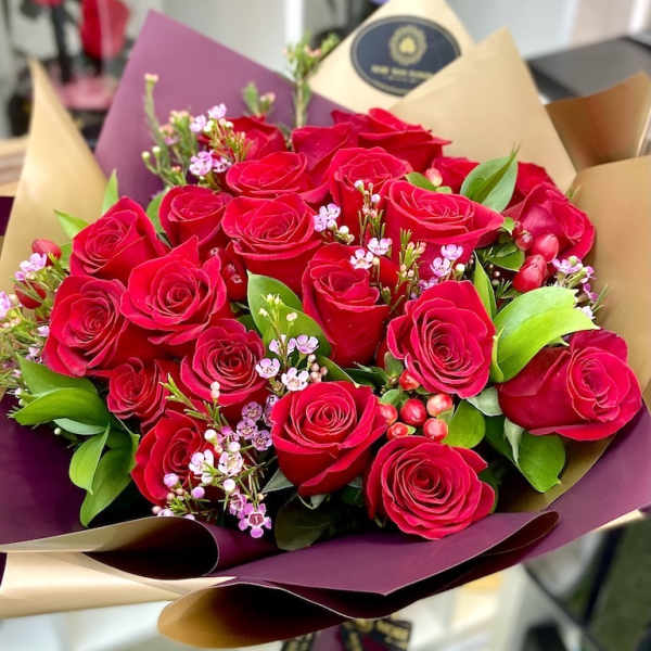 Large bouquet of red roses with small pink filler flowers wrapped in burgundy and tan paper
