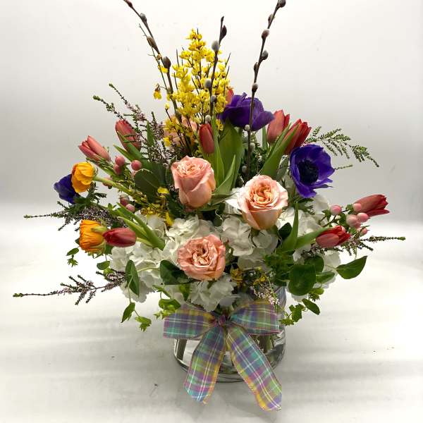 Mixed bouquet of roses, tulips, and hydrangeas in a glass vase with a plaid ribbon