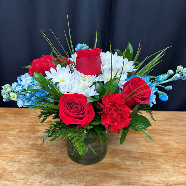 Red roses and white daisies in a glass vase with blue accents