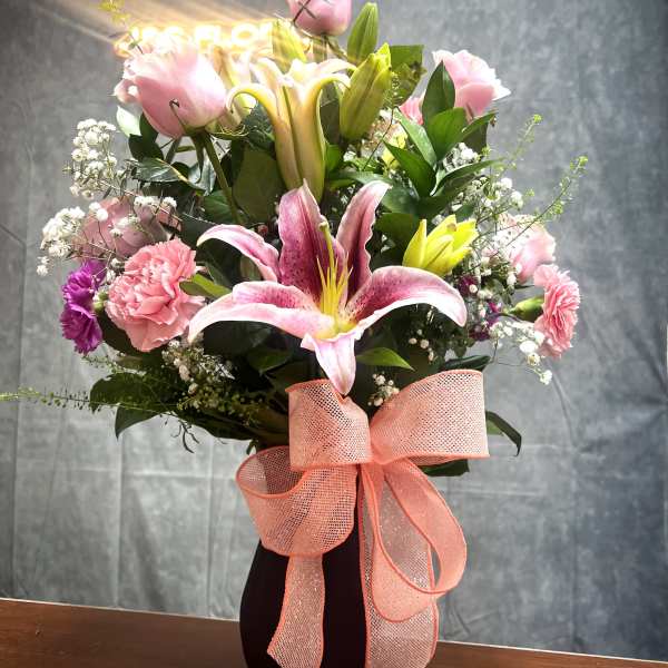 Pink lilies and carnations in a dark vase with a peach ribbon