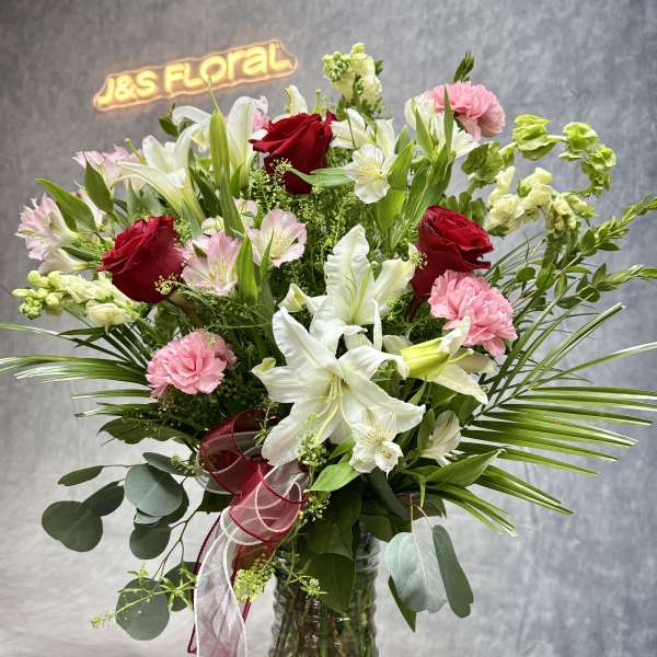Mixed bouquet of red roses, white lilies, and pink carnations in a glass vase