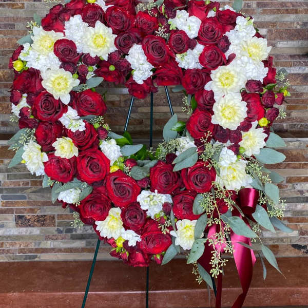 Heart-shaped floral wreath of red roses and white flowers on a stand