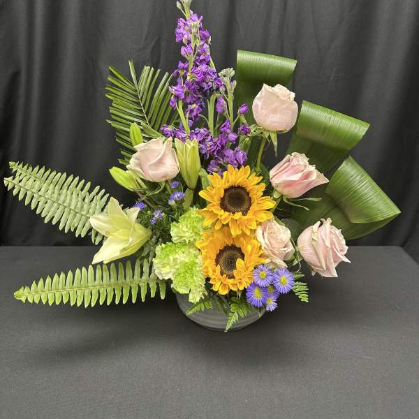 Mixed bouquet with pink roses, sunflowers, and purple flowers in a vase