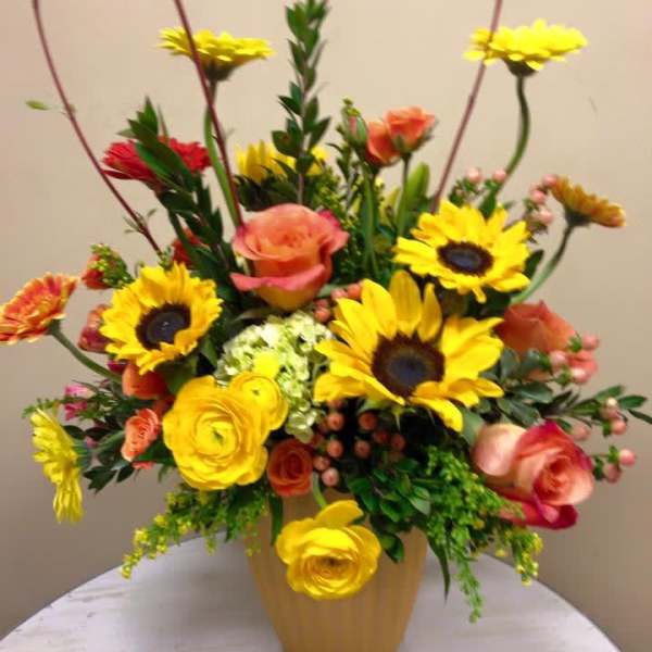 Bright mixed bouquet in a tan vase with sunflowers and roses