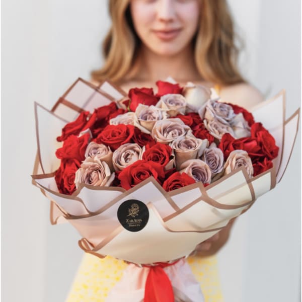 Large bouquet of red and blush roses wrapped in white paper with a red ribbon