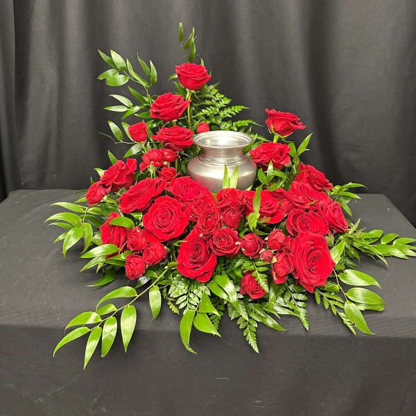 Red roses arranged around a silver urn on a black draped table