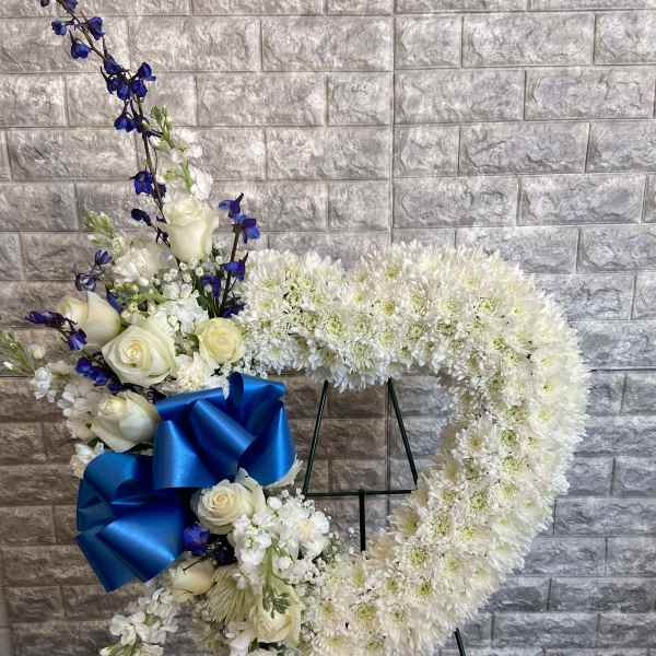 White floral heart wreath with blue ribbon on a stand