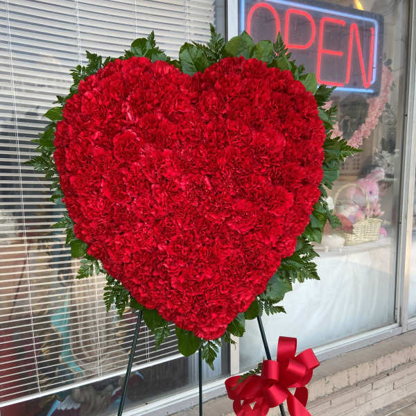 Heart-shaped red carnation standing spray with a ribbon on an easel
