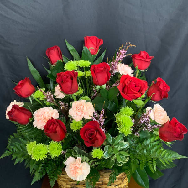 Basket arrangement of red roses, pale pink carnations, and green mums
