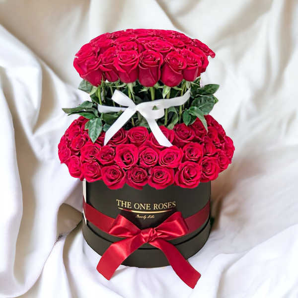 Two-tier arrangement of red roses in a black round box with ribbons