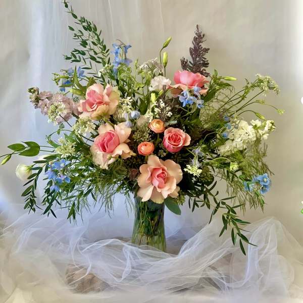 Tall mixed bouquet of pink roses and blue flowers in a glass vase