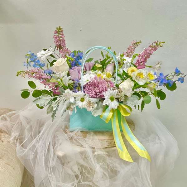 Pastel mixed flower arrangement in a turquoise basket with ribbon