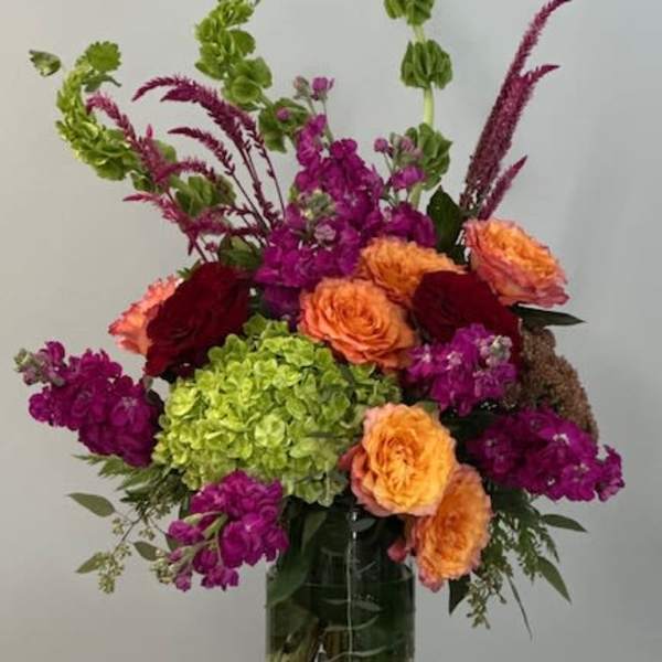 Tall mixed bouquet in a glass vase with orange, magenta, and green blooms
