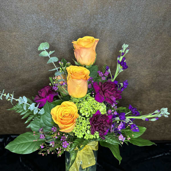 Orange roses and purple flowers in a glass vase with a yellow ribbon