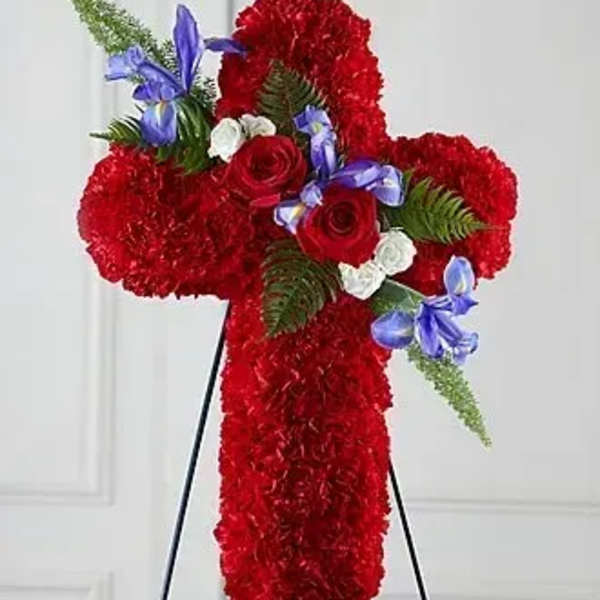 Standing red carnation cross with red roses, white blooms, and purple irises on a black easel