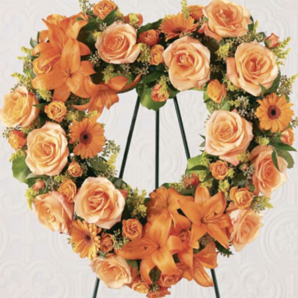 Heart-shaped floral wreath with orange roses and lilies on a stand