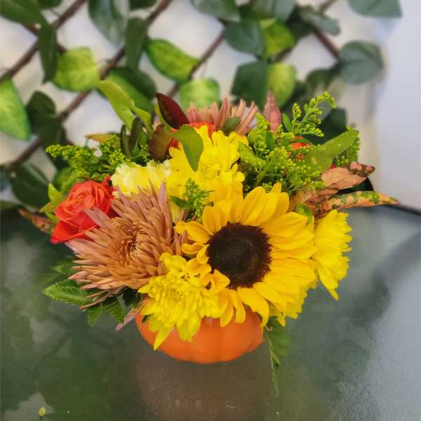 Mixed bouquet in an orange pumpkin container with sunflowers and roses