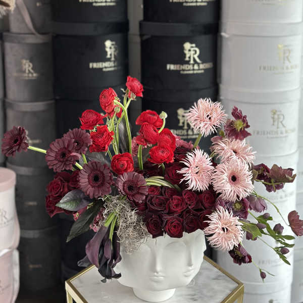 Mixed red, burgundy, and pale pink flowers in a white face vase