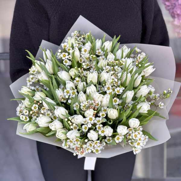 Bouquet of white tulips and small white flowers wrapped in pale paper