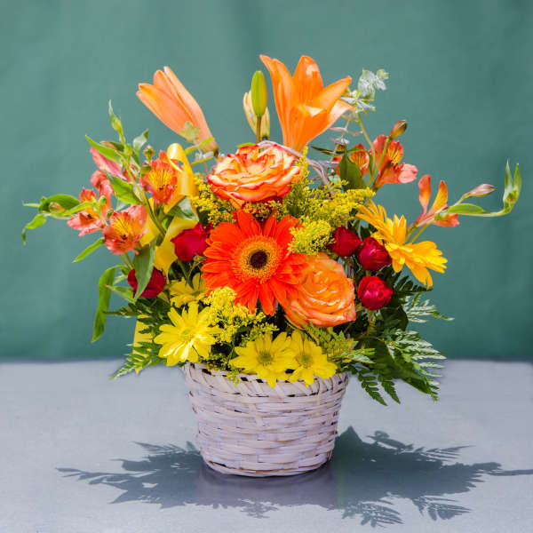 Mixed bouquet in a woven basket with orange, yellow, and red flowers