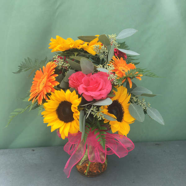 Bouquet of sunflowers, pink roses, and orange gerbera daisies in a glass vase
