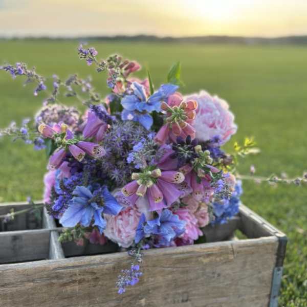 Mixed bouquet of blue, pink, and purple flowers in a wooden crate