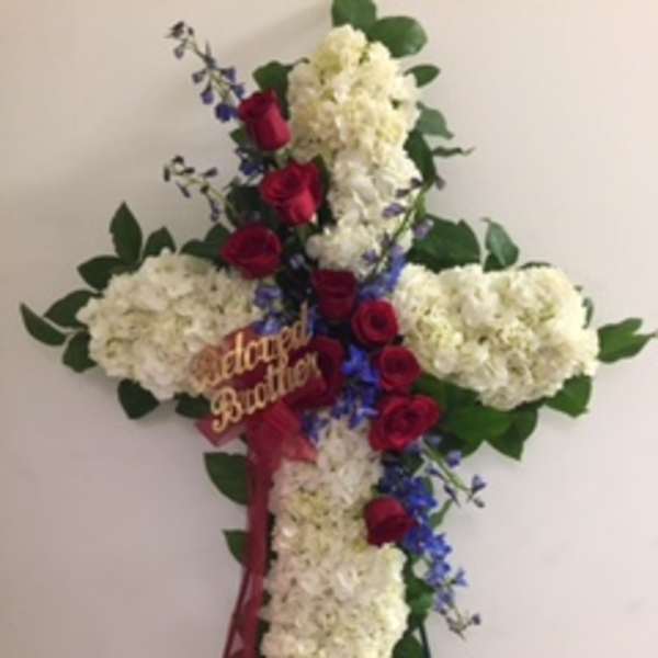 Cross-shaped floral tribute with white hydrangeas, red roses, and blue flowers