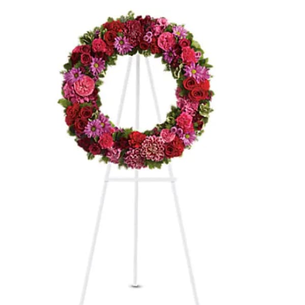 Circular floral wreath on a white easel with pink and red flowers