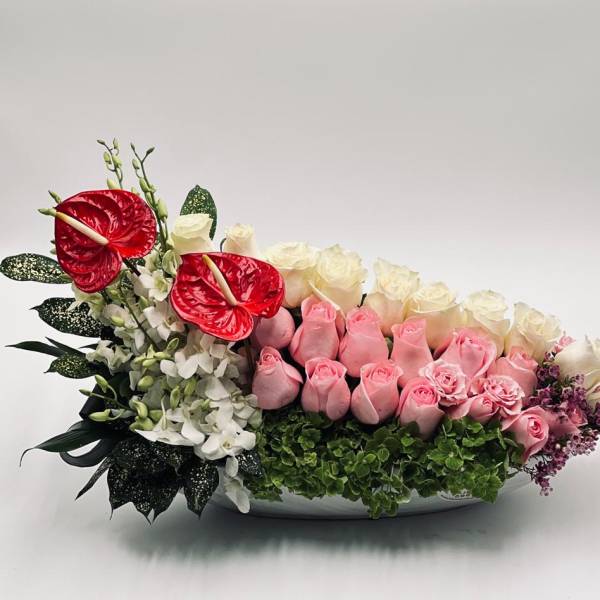 Pink and white roses with red anthuriums in a low white bowl