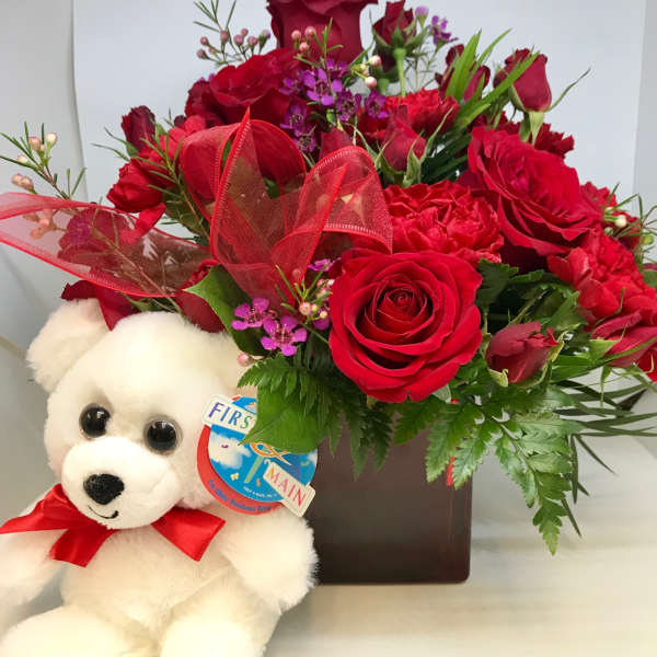 Red rose bouquet with a white teddy bear and ribbon in a square vase