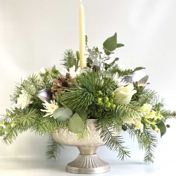 Pine and white floral centerpiece in a silver pedestal bowl with a tall candle