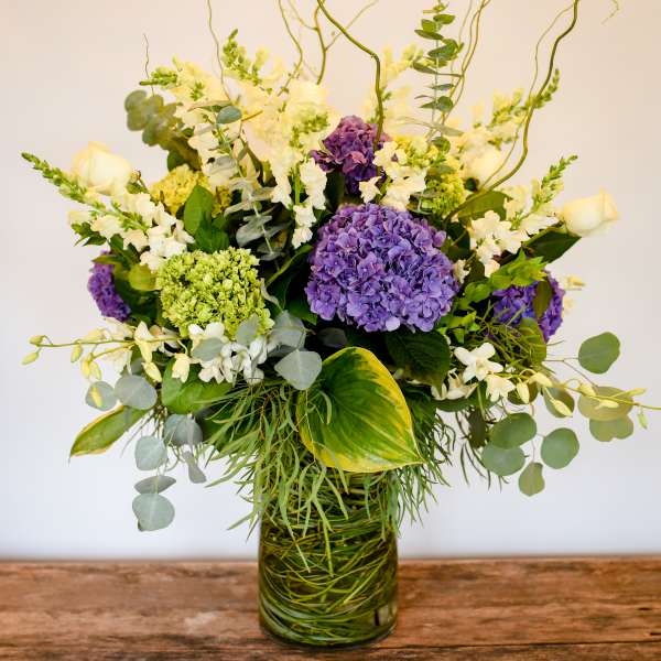 Purple hydrangeas and white flowers in a glass vase