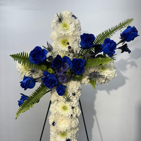Cross-shaped floral tribute with white chrysanthemums and blue roses on an easel