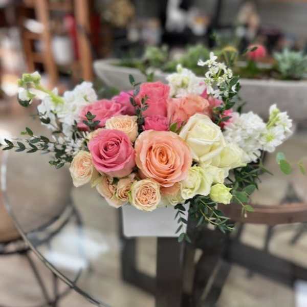 Pink and peach roses arranged with white flowers in a low centerpiece.