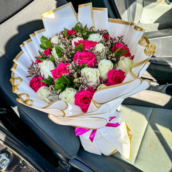 Bouquet of pink and white roses wrapped in white paper with gold trim