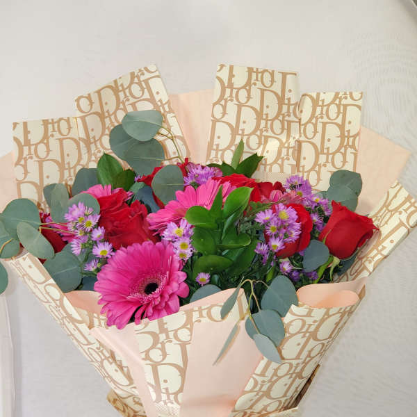 Hand-tied bouquet of red roses and pink gerbera daisies wrapped in branded cream paper