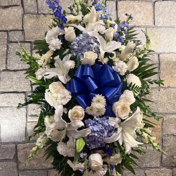 Standing floral spray with white lilies, roses, and blue flowers around a blue bow