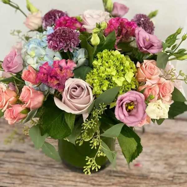 Mixed bouquet of pink, lavender, and peach blooms with green hydrangea in a green glass vase
