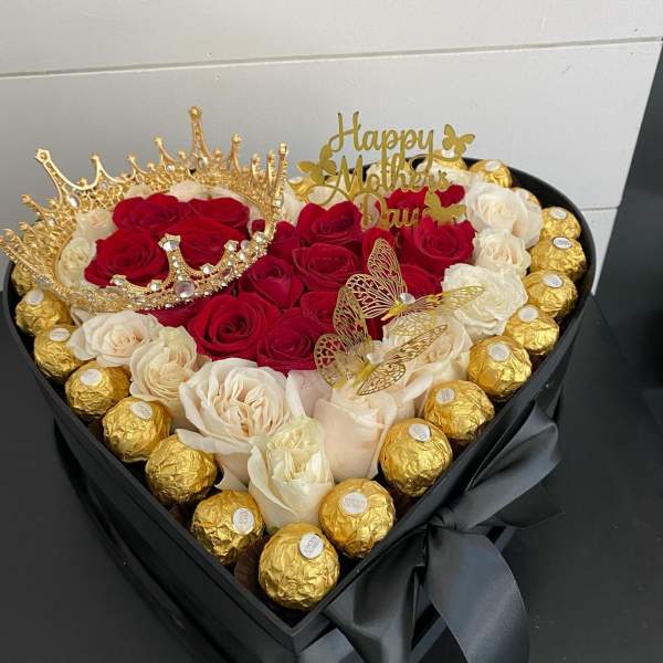 Heart-shaped box of red and white roses with gold chocolates and a crown topper