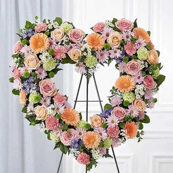 Heart-shaped floral wreath on a stand with pink, peach, and lavender blooms