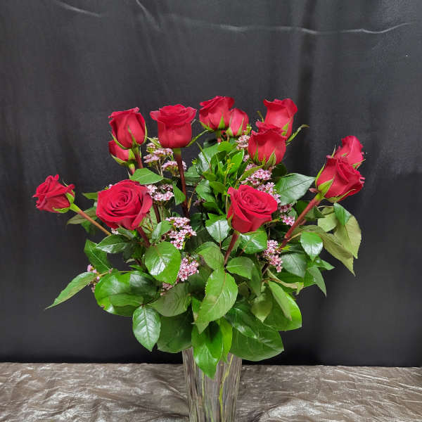 Red roses arranged in a clear glass vase with pink filler flowers