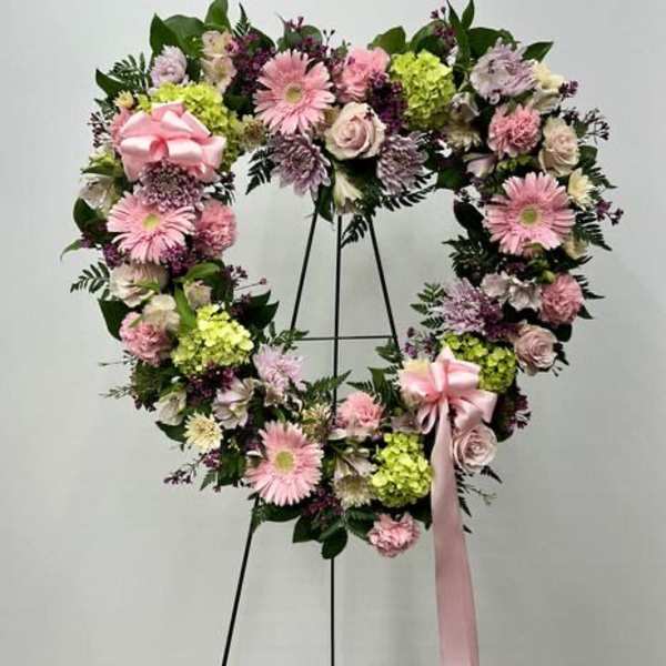 Heart-shaped floral wreath with pink flowers and a ribbon on a stand