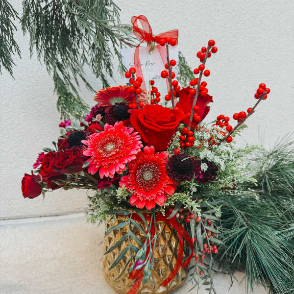 Red roses and gerbera daisies in a gold vase with berry stems