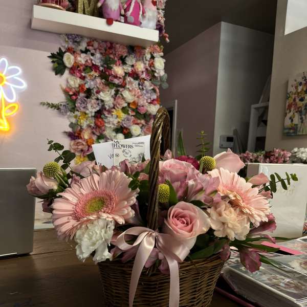 Pink flower arrangement in a wicker basket with a ribbon bow