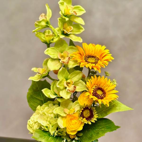 Yellow flowers and green orchids arranged in a pale vase