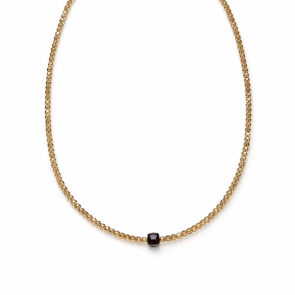 Gold beaded necklace with a small black pendant on a white background