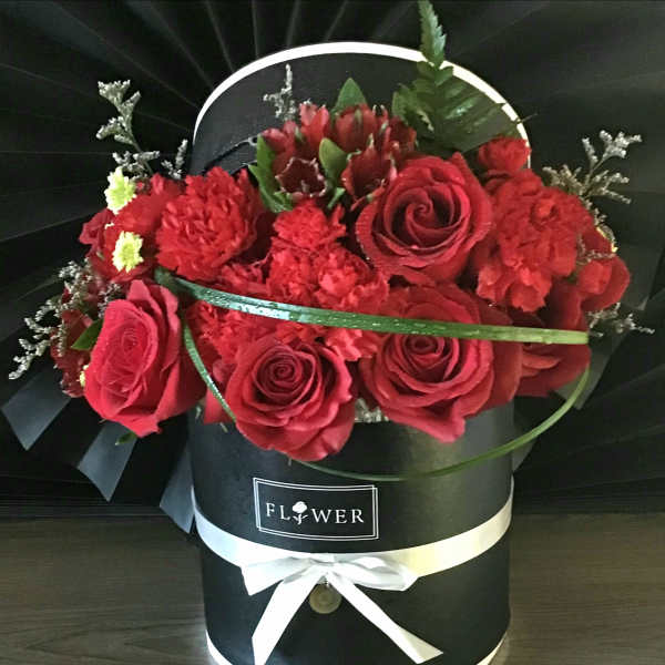 Red roses and carnations in a black hatbox with a white ribbon