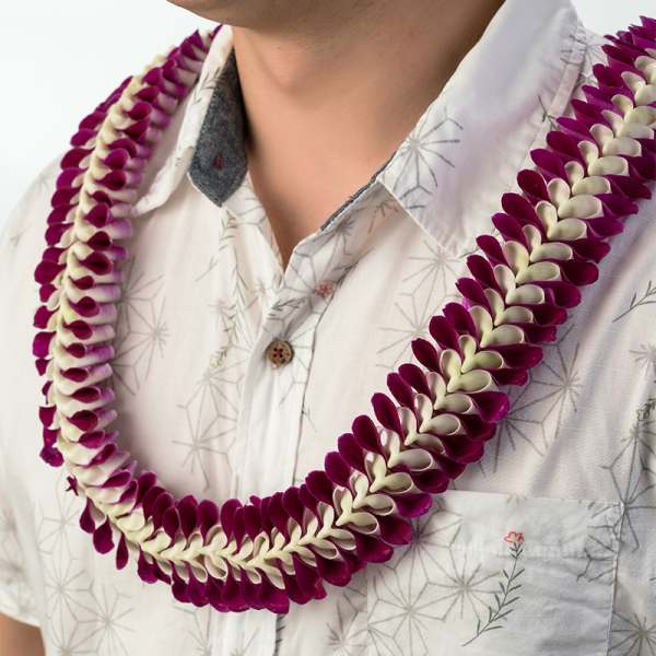 Purple and white orchid petal lei worn around a person’s neck over a patterned shirt