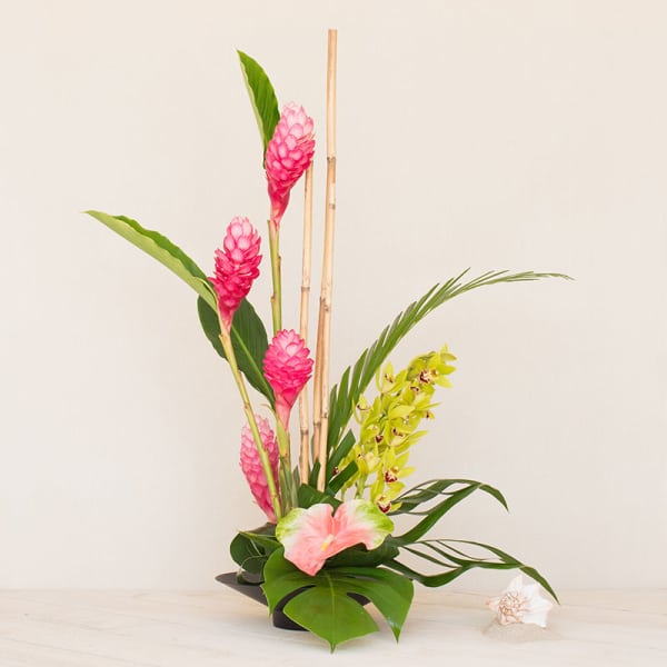 Tall tropical arrangement with pink flowers, green orchids, and bamboo in a black dish